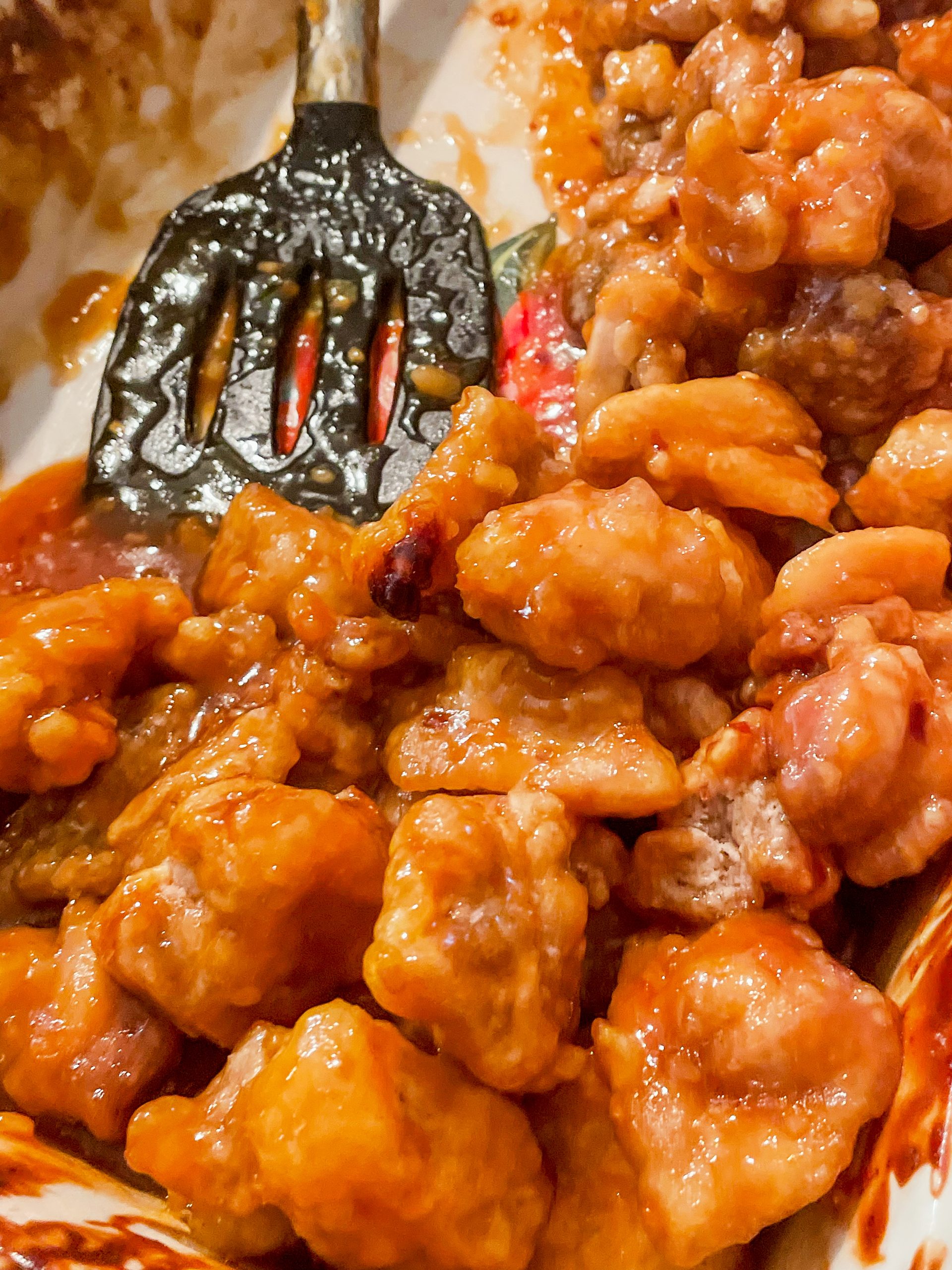 Orange chicken after being baked in a dish. The sauce is sticky, shiny, and coating the gluten free fried chicken. A Wonders of Cooking recipe