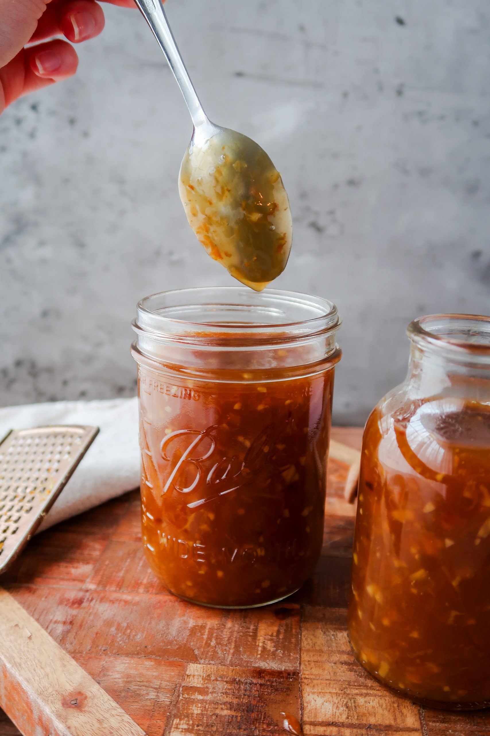 Homemade orange chicken saucing coating the back of a spoon to show viscosity. The sauce is in jars. A Wonders of Cooking recipe